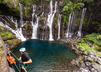 Homme se préparant à une descente en rappel sur une paroi pour du canyoning, devant de magnifiques cascades. Rivière Langevin, Réunion